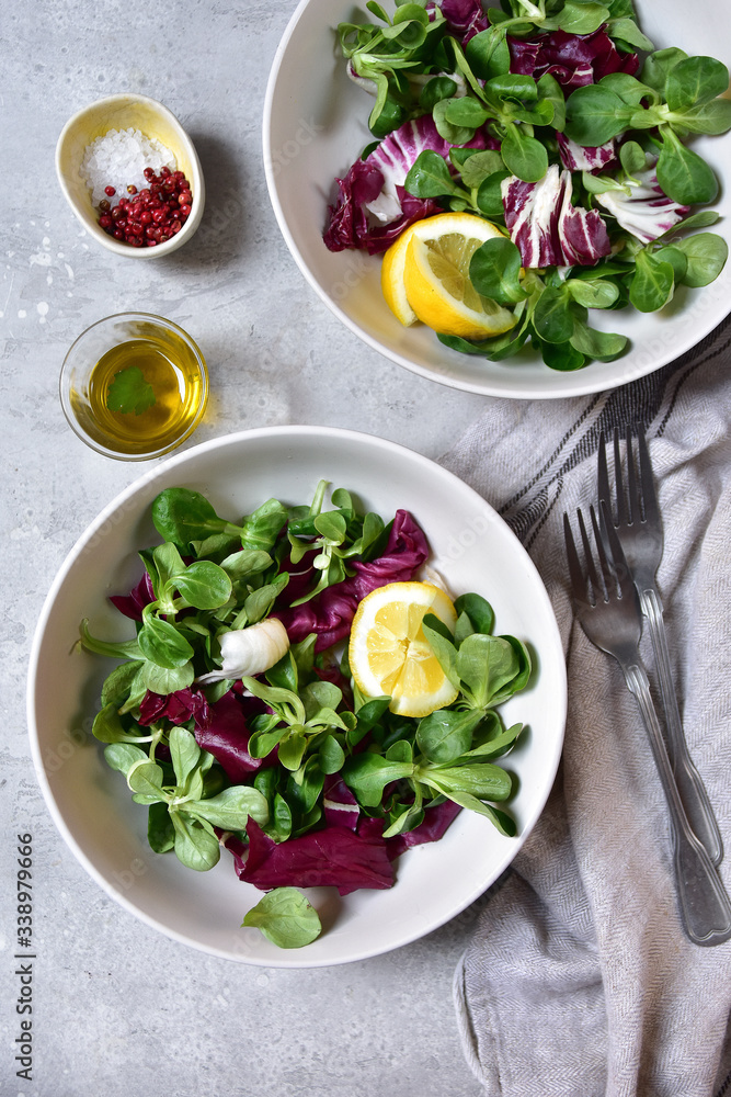 diet salad from radicchio, arugula, valerian leaves with lemon and olive oil in a white bowl on a gray background. vitamin diet salad recipe. selective focus, copy space