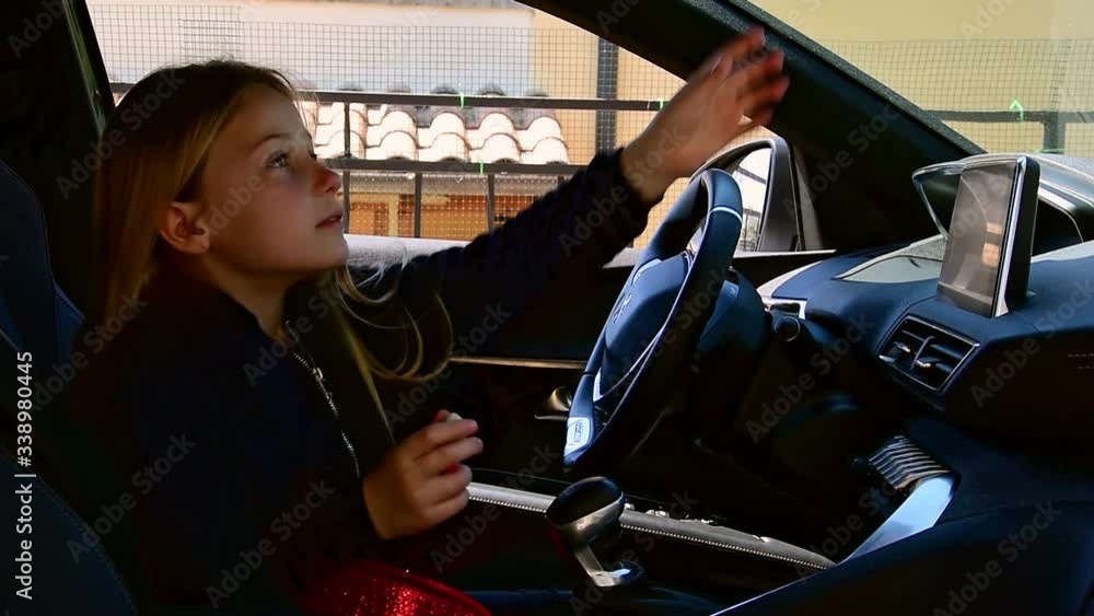 Cute little girl sits at the wheel of a standing car and paints her ...