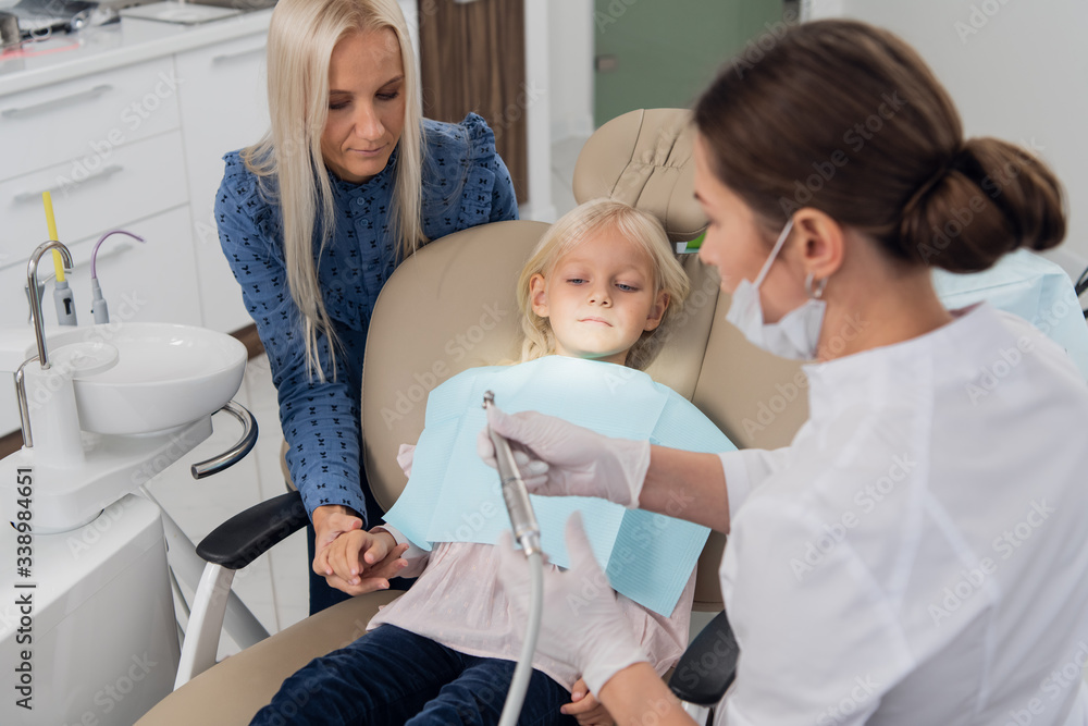 Fototapeta premium Beautiful mom and her cute little daughter at the dentists's, the girl is afraid of the drilling machine
