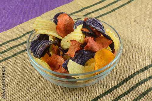 Vegetable chips made from yukon gold potatoes, blue potatoes, and sweet potatoes in glass snack bowl on place mat photo