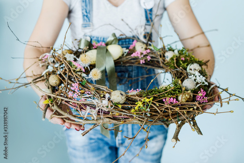 woman holding easter wreath with colorful eggs and ribbons on sky blue background