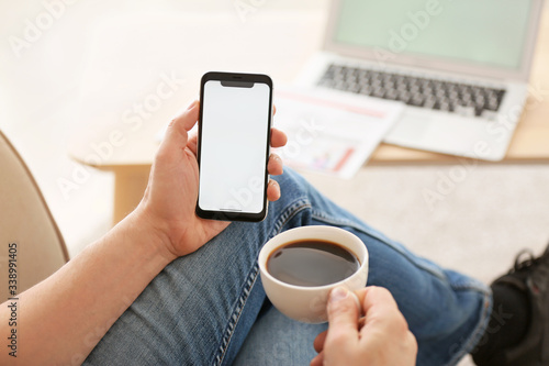 Young man with mobile phone drinking coffee at home