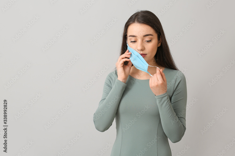 Young woman putting on medical mask against grey background Young woman putting on medical mask against grey background