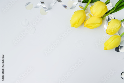 Yellow tulips and silner serpantine and confetti with space for text on grey background, flat lay, Happy Easter or woman concept. Mother greeting card photo