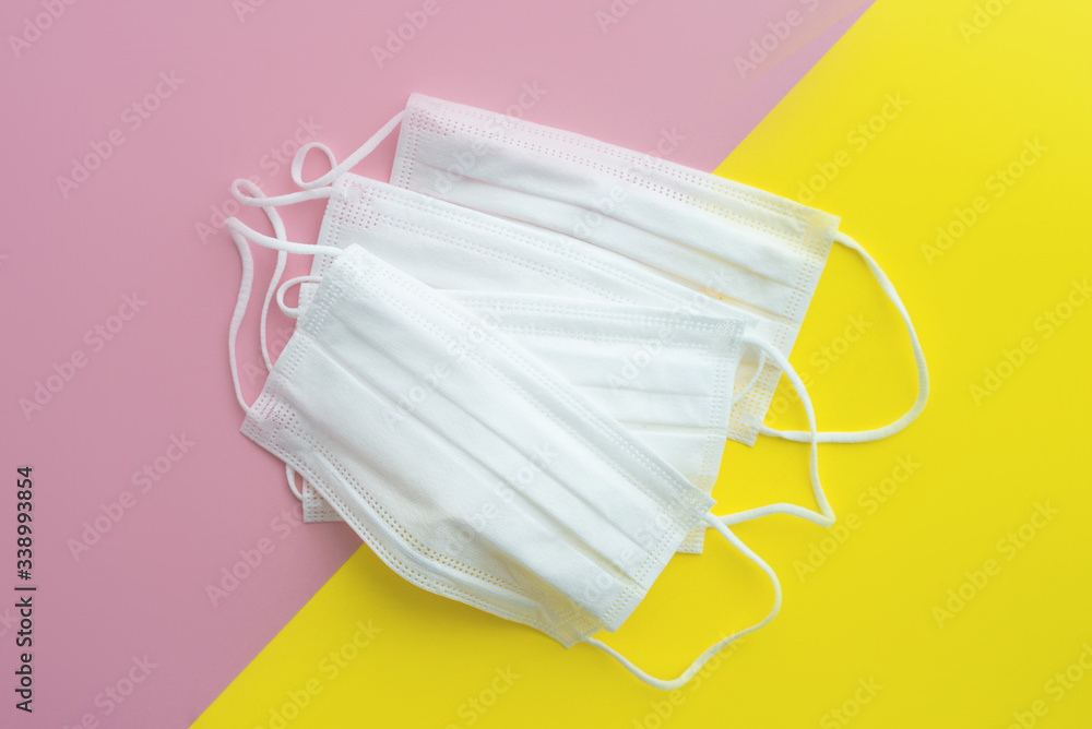 Collection of white medical mask. Yellow and pink background. Face mask protection against pollution, virus, flu and coronavirus. Health care concept. Selective foocus. Collection of white medical mask. Yellow and pink background. Face mask protection against pollution, virus, flu and coronavirus. Health care concept. Selective foocus.