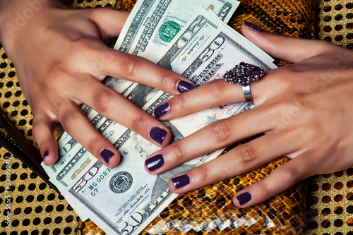 pretty fingers of african american woman holding money closeup with purse, luxury jewellery on python clutch, cash for gifts