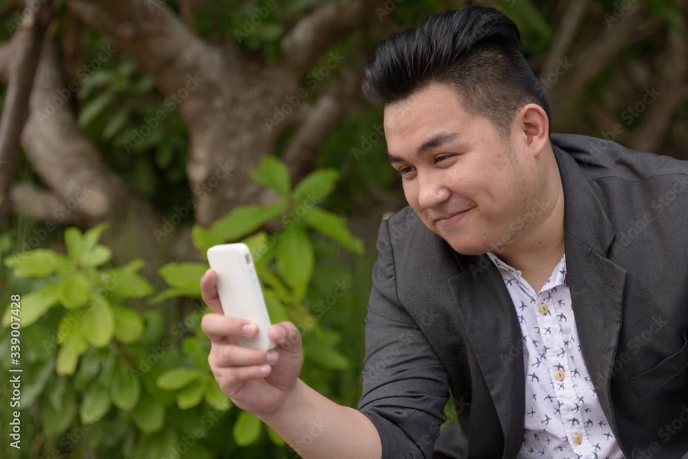 Young overweight Asian businessman using phone at the park Young overweight Asian businessman using phone at the park