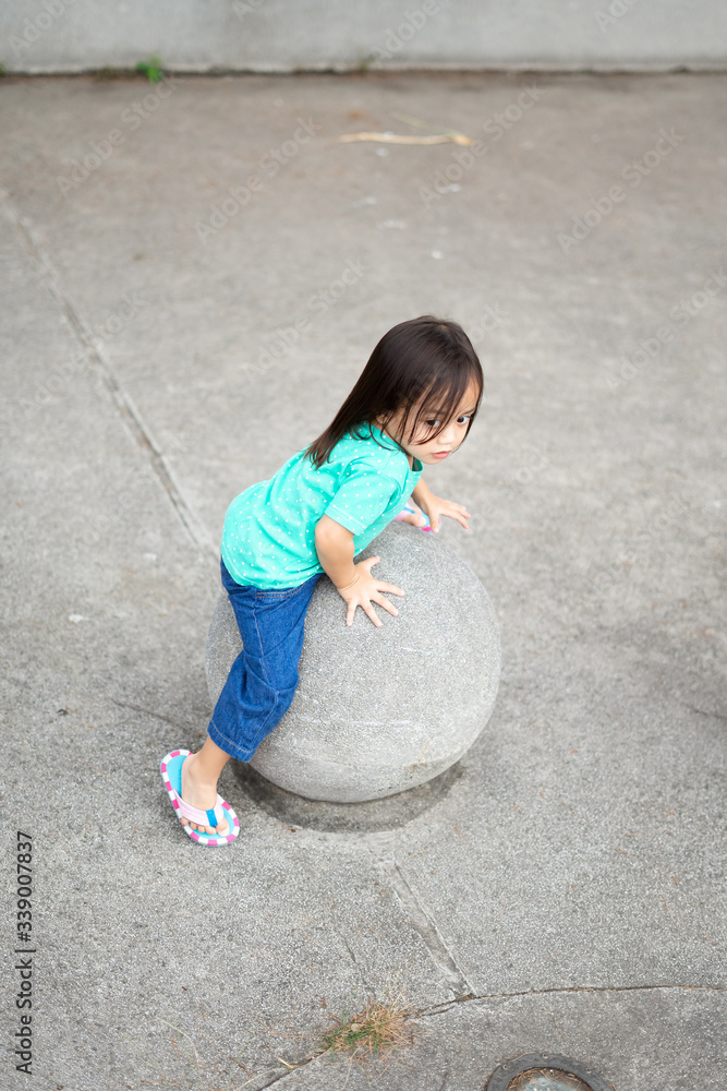 Naklejka premium A toddler child sitting on the concrete sphere ball shape in the park.