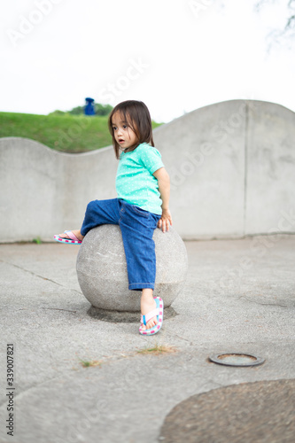 A toddler child sitting on the concrete sphere ball shape in the park.