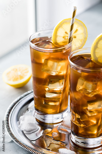 Very close up view of glasses of ice tea and lemon slices on a metal tray against a window sill.