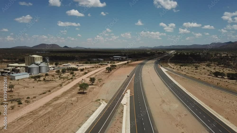 4K aerial video of newly upgraded main A1/B1 highway outside Windhoek to town Okahandja with bush covered mountains, dry endless savanna view, metal silo towers in Khomas Region, central Namibia 4K aerial video of newly upgraded main A1/B1 highway outside Windhoek to town Okahandja with bush covered mountains, dry endless savanna view, metal silo towers in Khomas Region, central Namibia