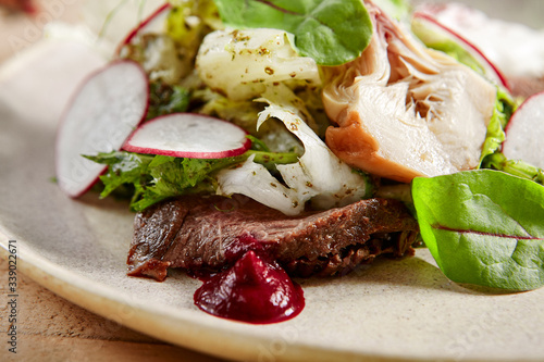 Roast beef, artichokes and poached egg salad in white plate closeup