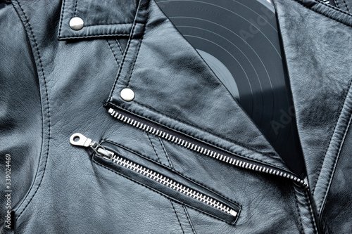 Closeup to a black leather biker jacket with LP vinyl disc. Music lover concept, retro photography.