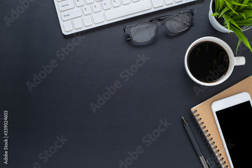 Workplace in office with black desk. Top view from above of keyboard with notebook and phone. Space for modern creative work of designer. Flat lay with blank copy space. Business and finance concept.