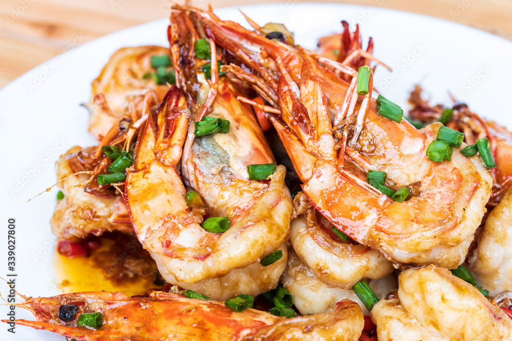 Closeup of Fried stir spicy shrimps on a white dish on wooden table. Special thai seafood. Thai Dish Cuisine. Thai food. Closeup of Fried stir spicy shrimps on a white dish on wooden table. Special thai seafood. Thai Dish Cuisine. Thai food.
