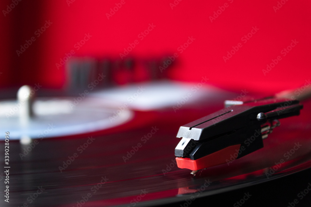 close up to a turn table needle playing a LP vinyl disc with turn table and red background. music lovers concept