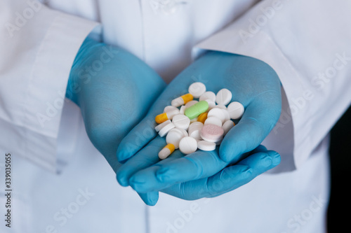 Many small white pills in the hands of a doctor wearing medical blue disposable gloves. Hands take one pills