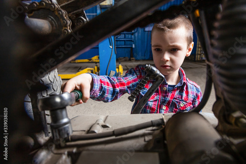 The boy dreams of becoming an adult and repairing cars. The boy, a young auto worker, unscrews the nuts with a wrench in the garage of a service station.