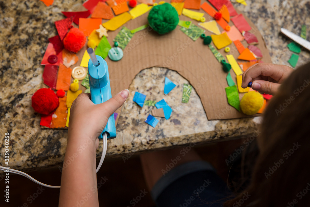 Fototapeta premium Child putting object on a rainbow collage while holding a hot glue gun