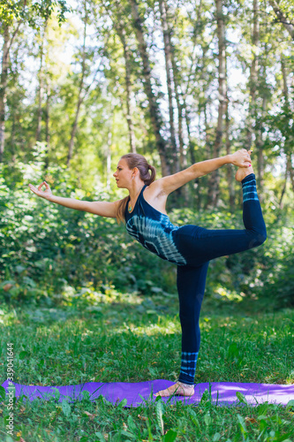 Young woman doing yoga exercises in summer city park.