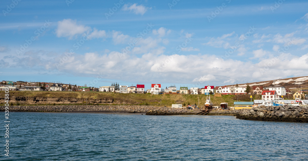 Panorama shot from the sea towards the charming city of Husavik in northern Iceland. Houses and snow covered mountains during spring time.