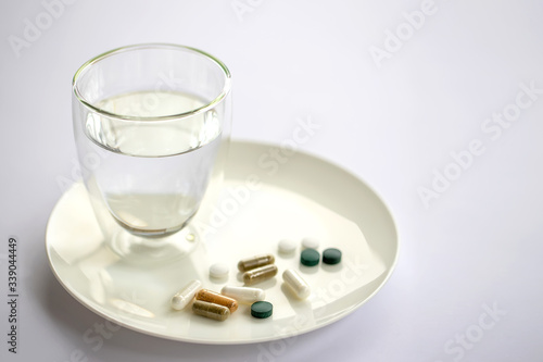 Glass of water and pills on a plate isolated on white. Medicine and health concept.