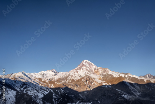 Mount Kazbek in the snow and the village of Stepantsminda in Georgia. Dawn in the mountains and the peak of Kazbek illuminated by the sun with sparkling snow on top.