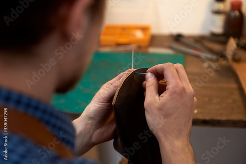 The leatherman threading needle for leather working. Closeup of male hands sewing leather parts with needle. The master with his own hands makes leather goods at his desk.