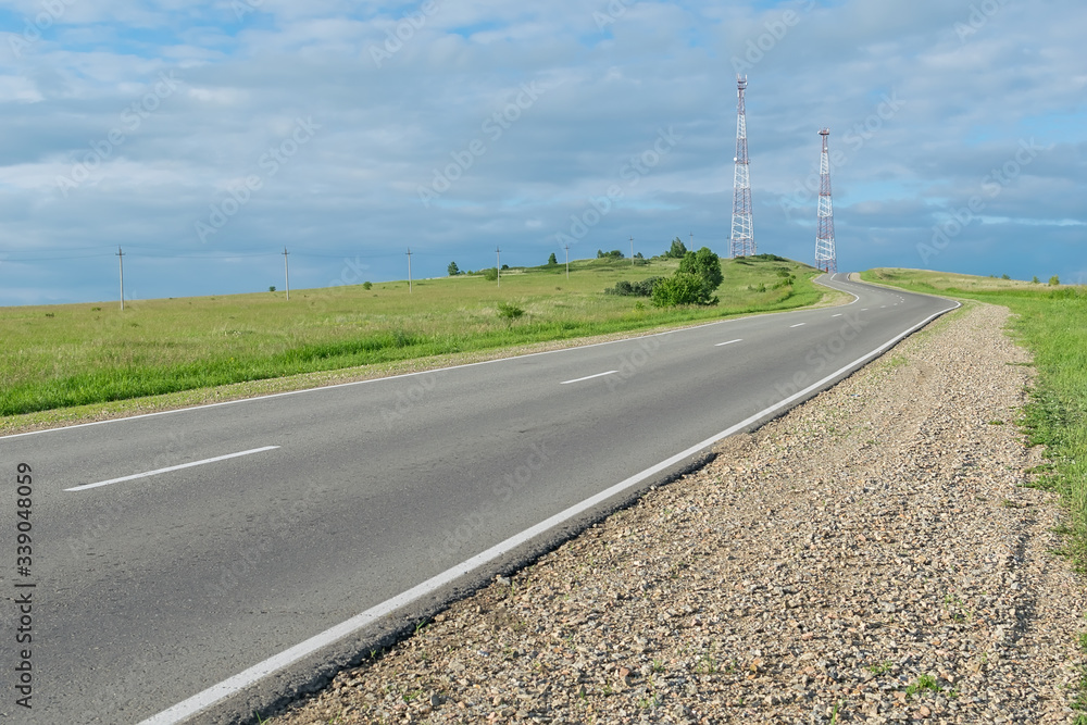 a asphalt country road that runs uphill and has cellular telecommunications towers