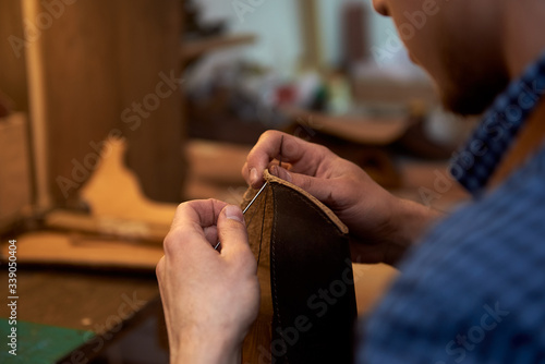 Closeup male hands threading needle for leather working. An artisan working with brown leather, needle and thread. Сlose-up of a needle with a thread in the hands of a master of genuine leather.