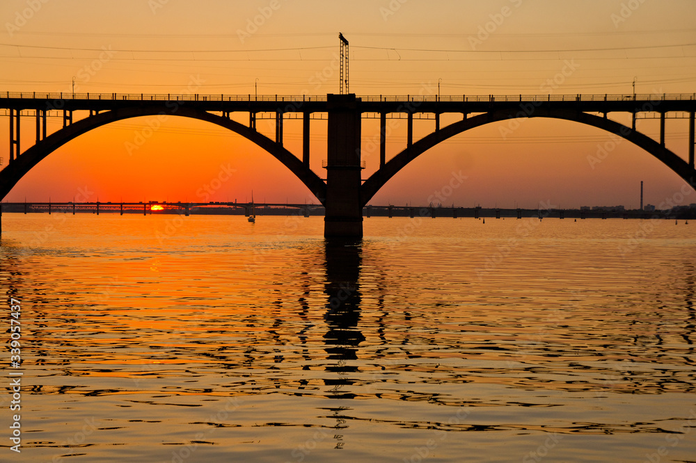 Fototapeta premium A bridge on a river lit by the sun at sunset. Evening river landscape.