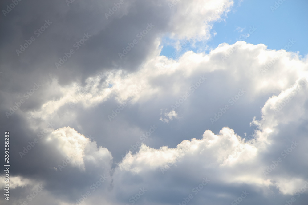 A piece of blue sky is visible between huge cumulus clouds. The edges of the clouds are illuminated by sunlight. Theme of beautiful landscapes.