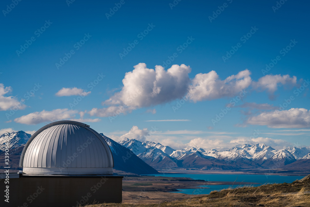 Bird’s eye view from Mt St John Observatory, with a view of the observatory dome, grassy hill overlooking a lake below with snow capped mountains in the background in Tekapo in New Zealand South Islan
