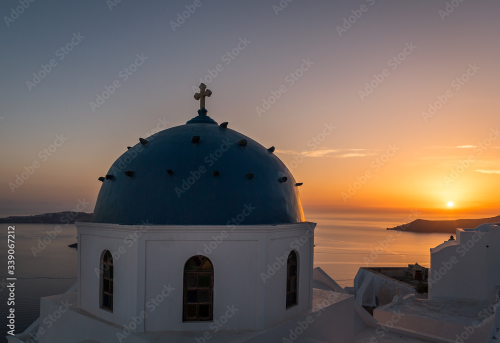 Obraz premium A beautiful golden sunset overlooking a church in Imerovigli, Santorini. 