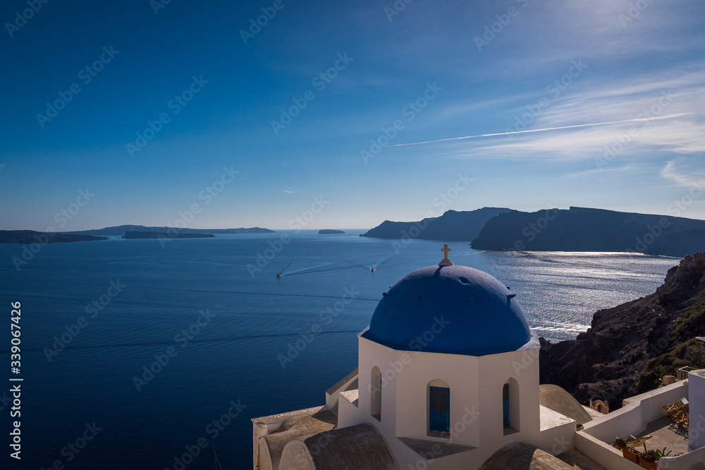 Overlooking the beautiful blue Caldera ocean with the famous blue dome churches of Oia in the foreground in Santorini, Greece. 
