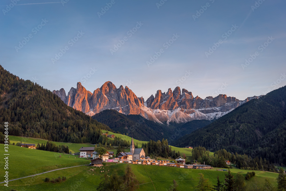 Sunset over the church of St. Magdalena in the Vilnoss Valley in Val di Funes with a view of The Dolomites Geisler Odle mountain peaks in the background. A beautiful town in South Tyrol, Norther Italy