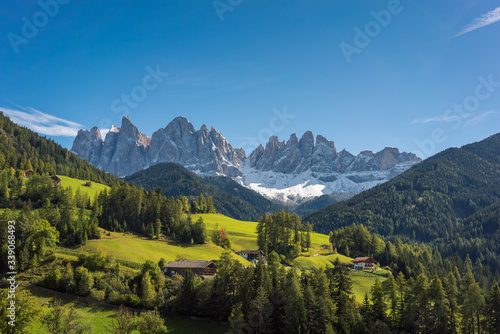 A scenic view overlooking a beautiful valley with surrounding forest and countryside and The Dolomites Geisler Odle mountain peaks in the background. Located in San Pietro, South Tyrol, Italy © Matthew