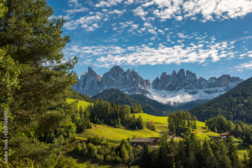 A scenic view overlooking a beautiful valley with surrounding forest and countryside and The Dolomites Geisler Odle mountain peaks in the background. Located in San Pietro, South Tyrol, Italy