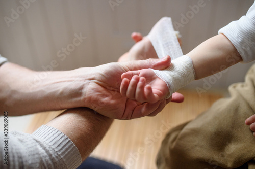 Father putting bandage on small hurt toddler child indoors at home.
