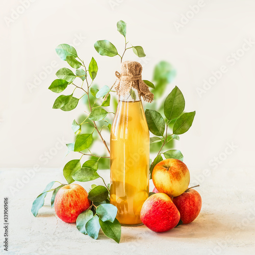 Εκτύπωση καμβά Homemade apple juice in glass bottle standing on white table with red apples and green leaves at white wall background