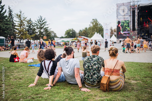 Rear view of group of young friends sitting at summer festival.