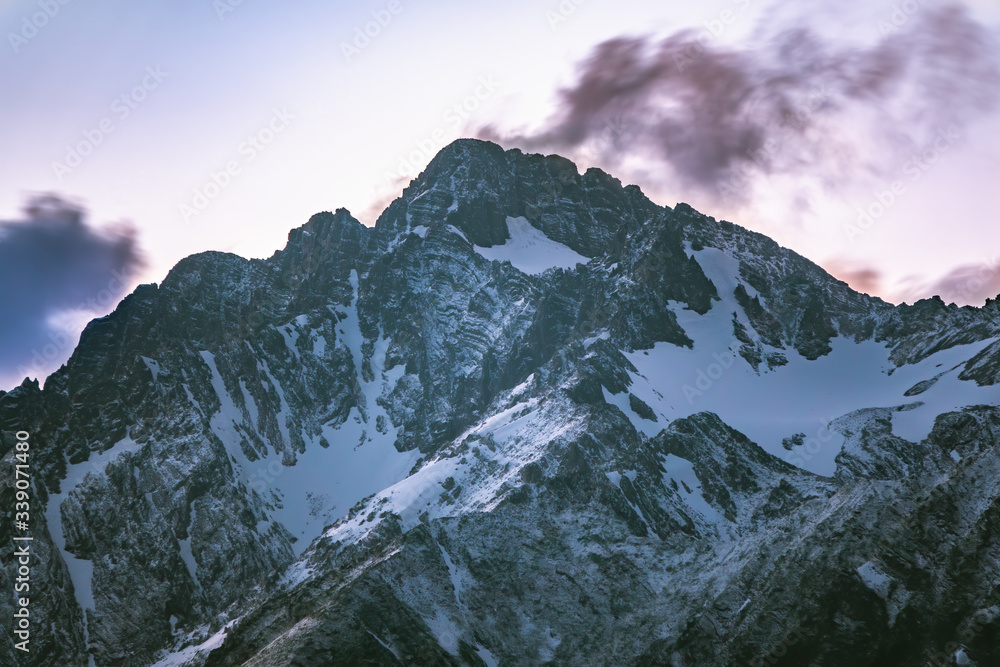 Obraz premium High mountains with snowy peaks at sunset in clouds and fog