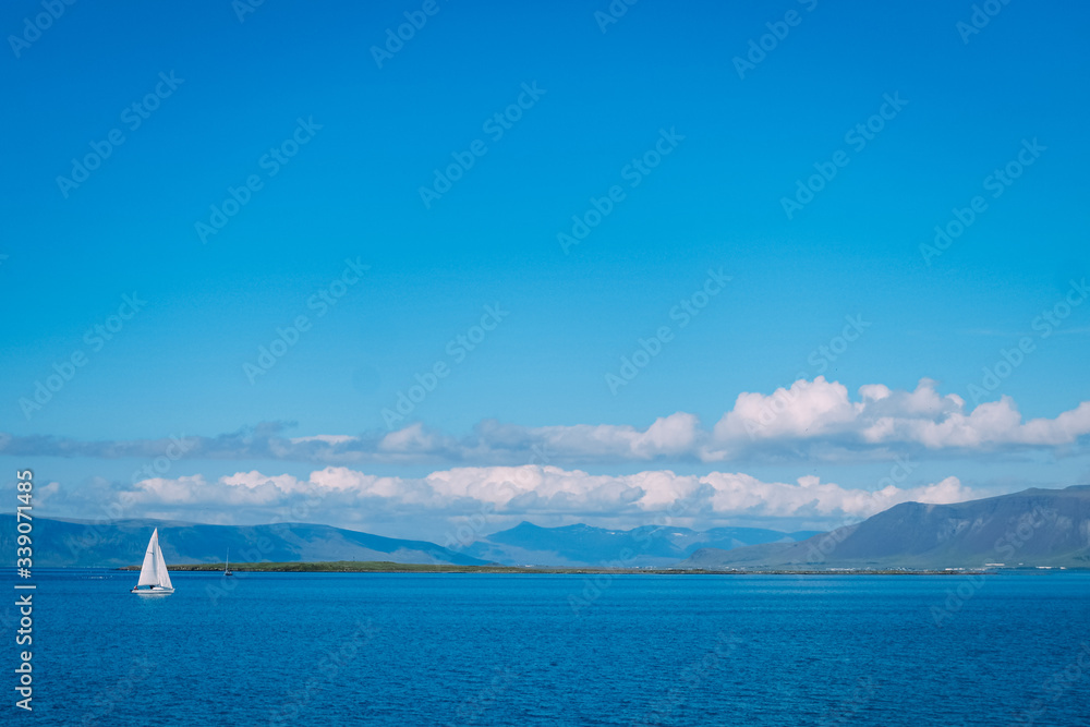 white yacht with a white sail in the distance in the Reykjavik fjord on a sunny summer day and a lot of clouds