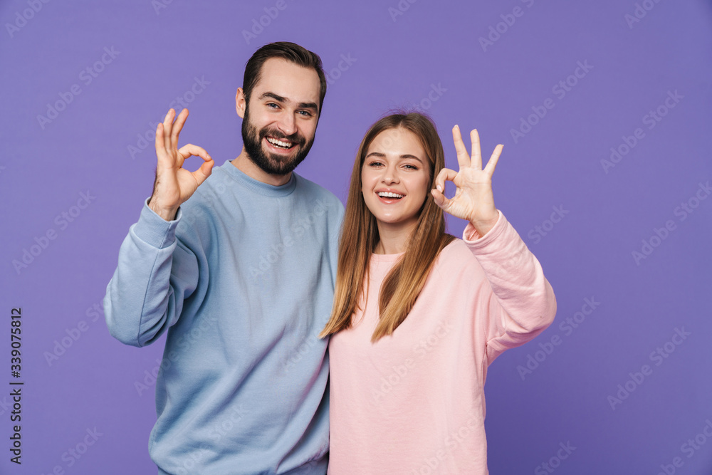 Smiling young loving couple showing okay gesture.