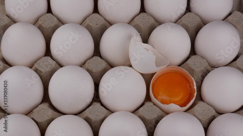 Chicken eggs in tray, in which one broken so that you can see a bright yolk and shell closeup