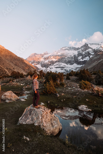 Tajikistan. Fann mountains Summer. A girl in hiking clothes is standing on a large room and watching the mountains in the snow.