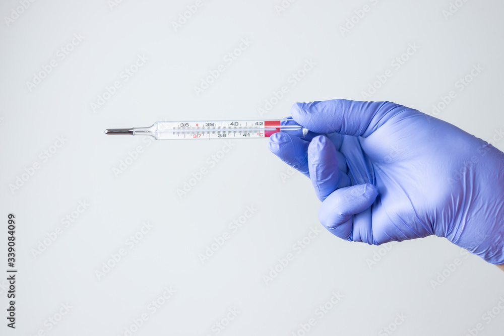 woman's hand with blue latex glove holding thermometer woman's hand with blue latex glove holding thermometer