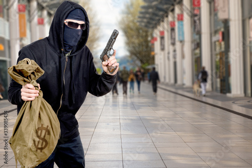 Fotografie, Obraz hooded robber with gun and bag of money in the city