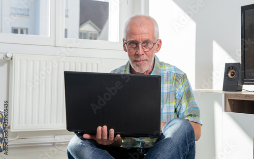 Senior with grey hairs wearing eyeglasses holding laptop