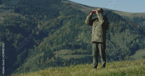 The hunter raised his binoculars, looking for his next destination in the mountains, The general plan